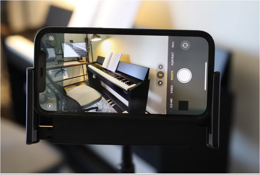 Phone on a stand showing a side-view camera angle of a digital piano — ideal for online piano lessons